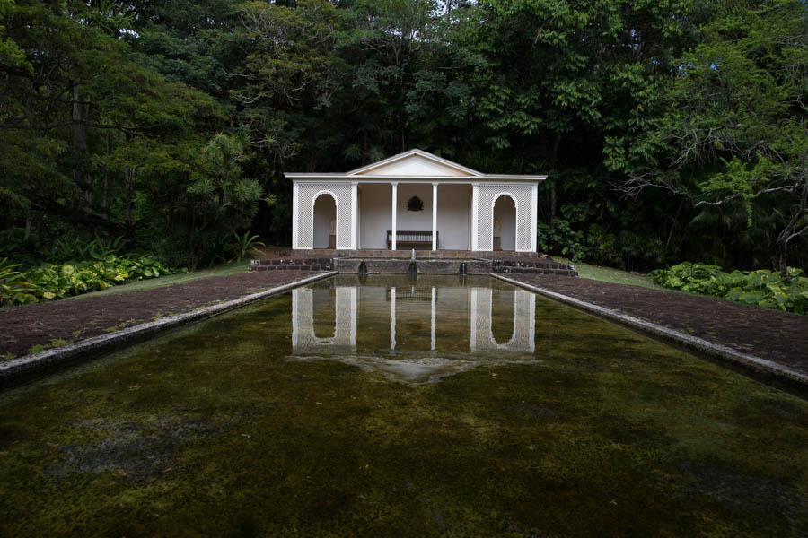A white neoclassical pavilion mirrored in a still reflecting pond, Allerton Garden, Kauai
