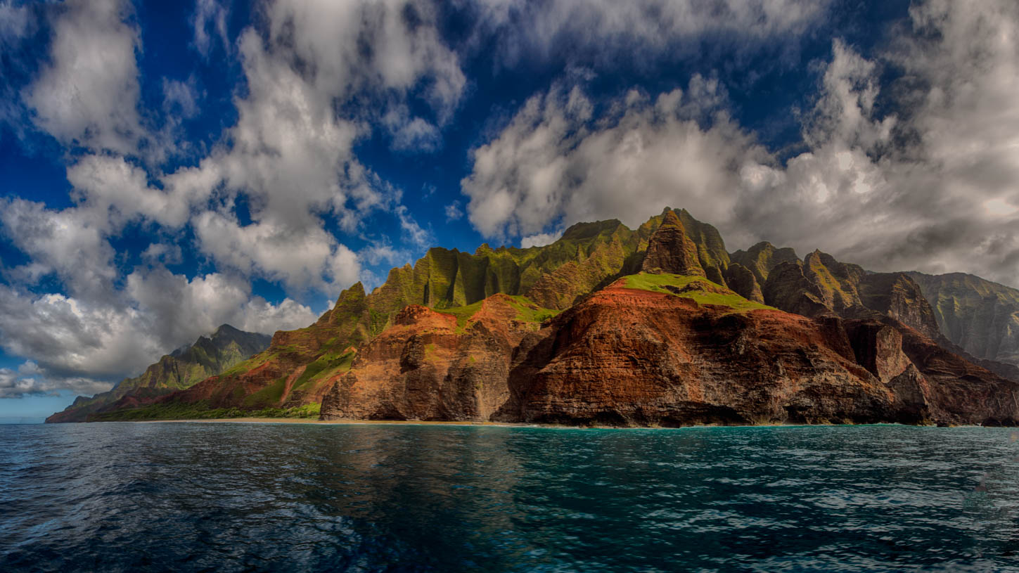 A headland rising straight out of the sea under stacked cloud, seen from the water, Kauai