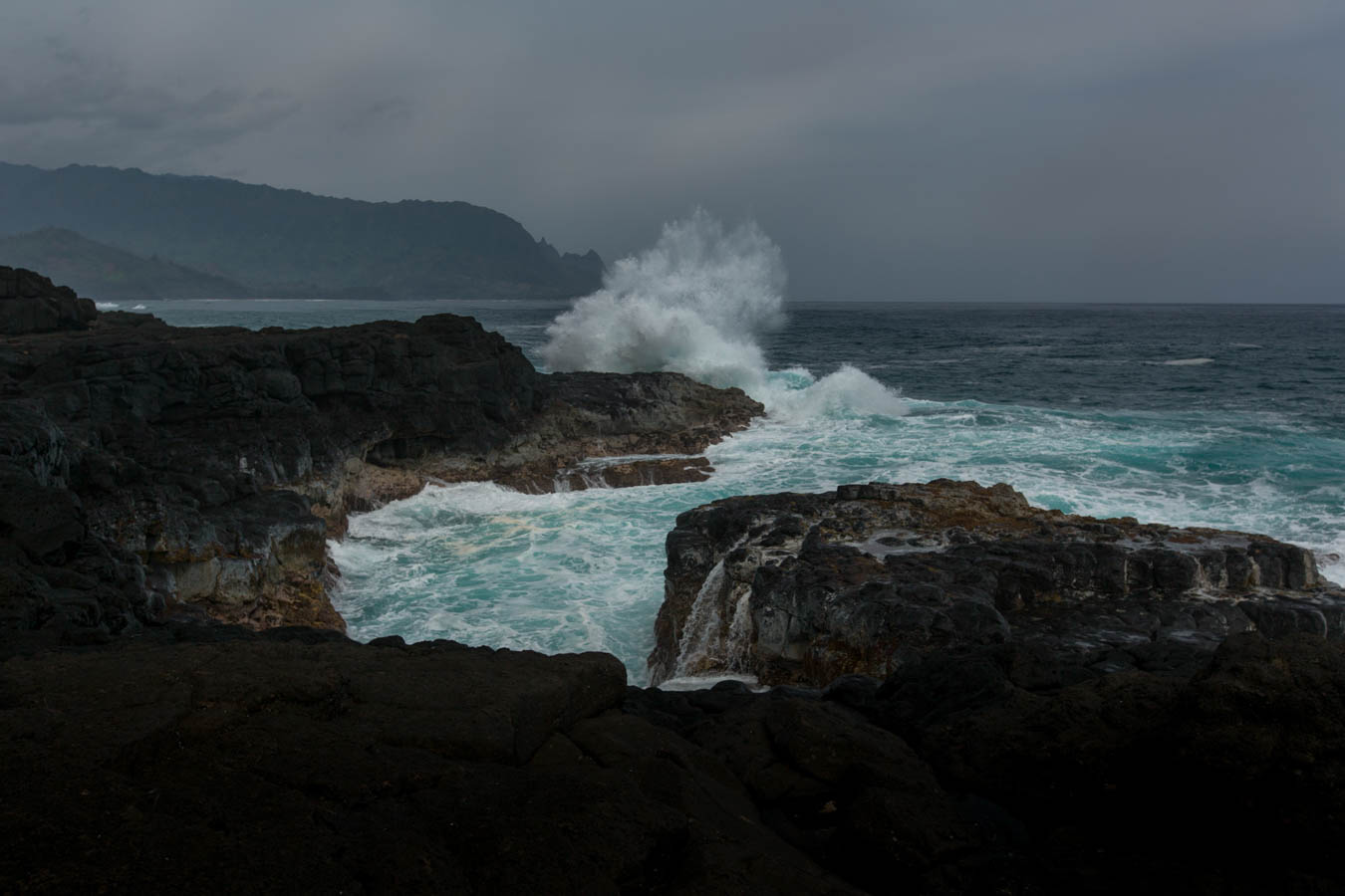 Surf breaking white over dark lava shelf with the north shore headland behind, Kauai