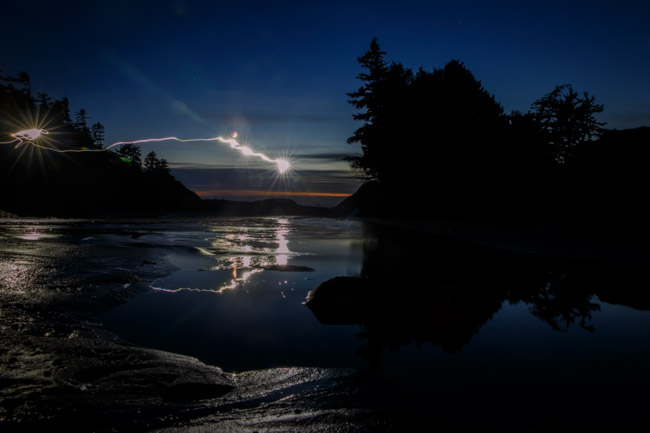 A long exposure at night, light drawn across still water with the treeline in silhouette, Tofino