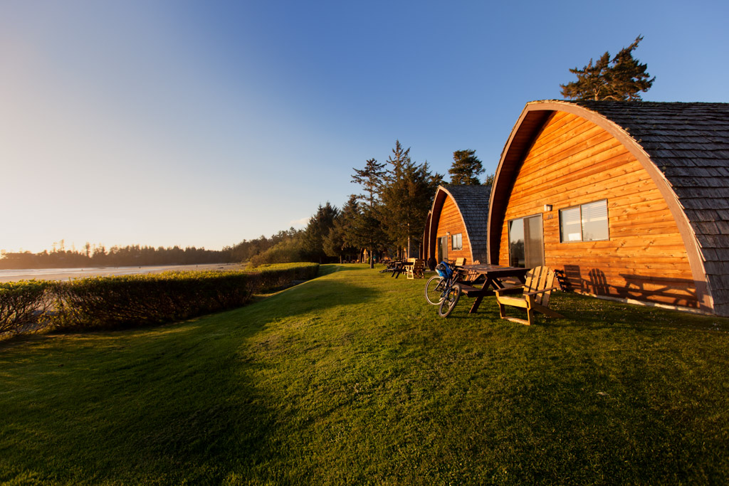 The arched cedar cabins at Ocean Village on cut grass, low sun behind the treeline, Tofino