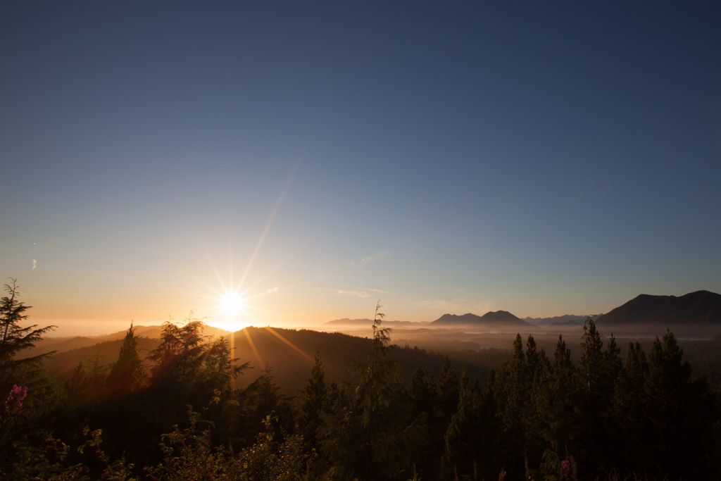 The sun on the horizon beyond layered ridgelines and the open Pacific, Tofino